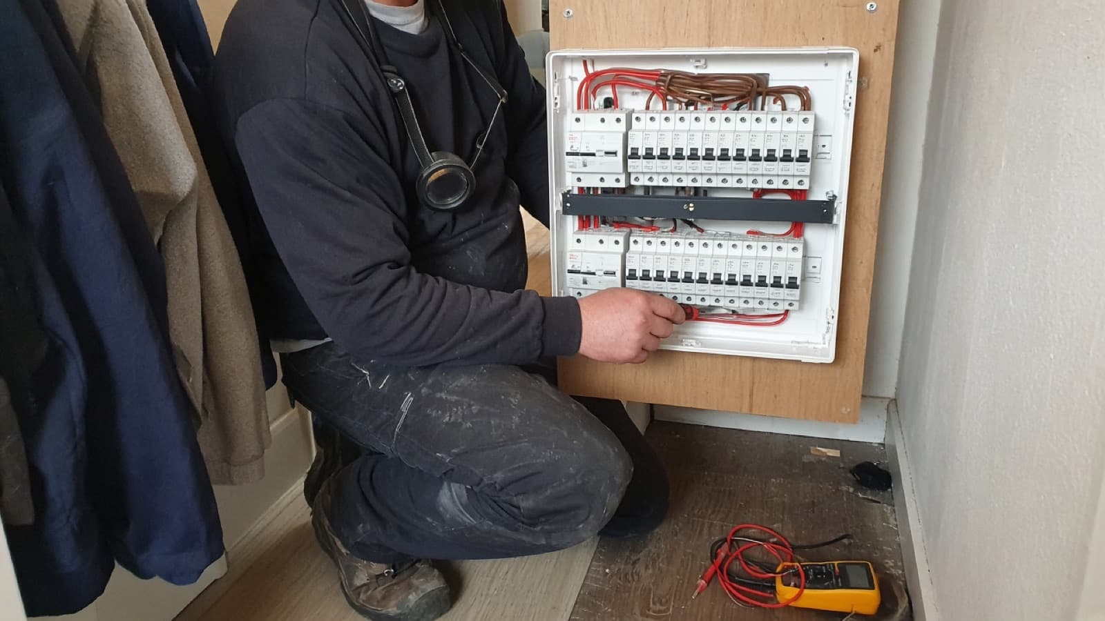 Electrician testing a domestic consumer unit in a hallway cupboard
