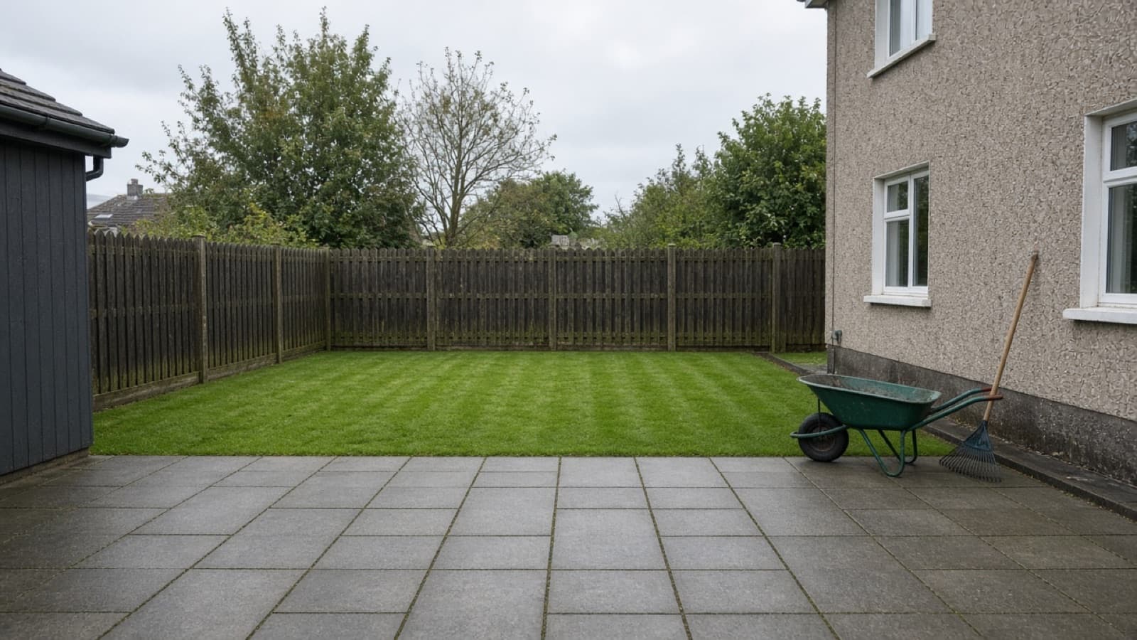 Back garden with fresh lawn, paving, and a wheelbarrow by the fence